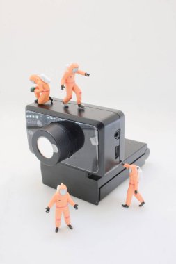 turuncu giyimli astronot figürleri küçük bir kamera aygıtı keşfediyor