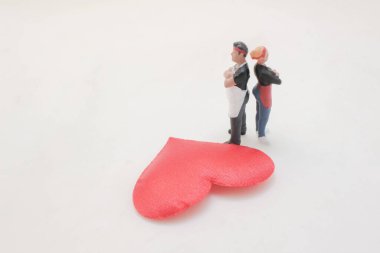 Parlak kırmızı bir kalbin yanında kollarını kavuşturmuş dur.