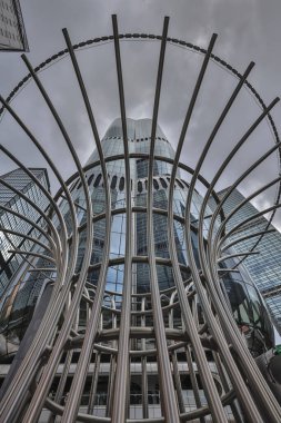 A towering glass skyscraper rises behind a dramatic spiral stainless