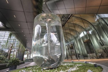 Modern bir şehir avlusunda uzun camdan bir sütun çeşmesi duruyor.,