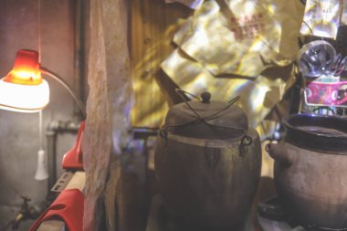 Warm, intimate workshop scene with clay pots on a green gas burner,