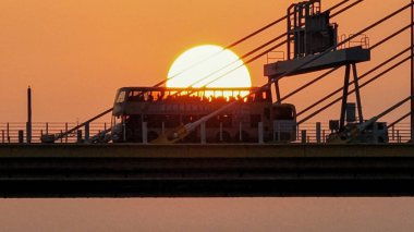 Dramatik bir günbatımı sıcak turuncu ışığı şehir köprüsünün üzerine saçar.