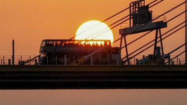Dramatik bir günbatımı sıcak turuncu ışığı şehir köprüsünün üzerine saçar.