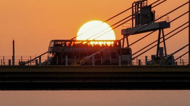 Dramatik bir günbatımı sıcak turuncu ışığı şehir köprüsünün üzerine saçar.