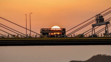 Dramatik bir günbatımı sıcak turuncu ışığı şehir köprüsünün üzerine saçar.
