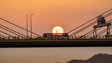 Dramatik bir günbatımı sıcak turuncu ışığı şehir köprüsünün üzerine saçar.