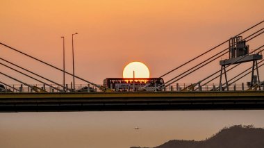 Dramatik bir günbatımı sıcak turuncu ışığı şehir köprüsünün üzerine saçar.