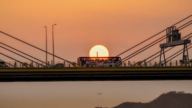Dramatik bir günbatımı sıcak turuncu ışığı şehir köprüsünün üzerine saçar.