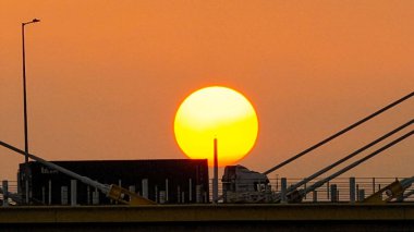 Kablolu bir köprünün arkasında sıcak bir günbatımı çarpıcı siluetler yaratır.