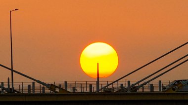 Kablolu bir köprünün arkasında sıcak bir günbatımı çarpıcı siluetler yaratır.