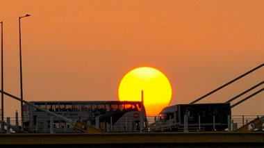 Kablolu bir köprünün arkasında sıcak bir günbatımı çarpıcı siluetler yaratır.