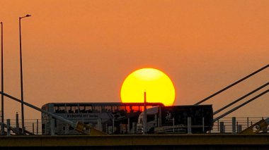 Kablolu bir köprünün arkasında sıcak bir günbatımı çarpıcı siluetler yaratır.