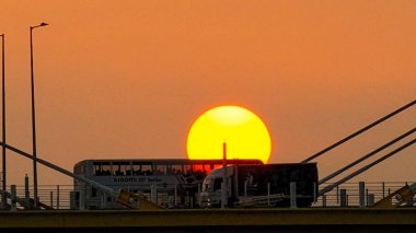 Kablolu bir köprünün arkasında sıcak bir günbatımı çarpıcı siluetler yaratır.