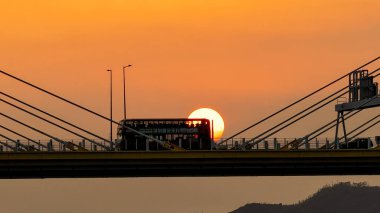 Dramatik bir günbatımı sıcak turuncu ışığı şehir köprüsünün üzerine saçar.