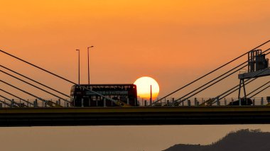 Dramatik bir günbatımı sıcak turuncu ışığı şehir köprüsünün üzerine saçar.