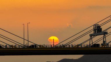 Dramatik bir günbatımı sıcak turuncu ışığı şehir köprüsünün üzerine saçar.