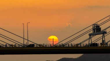 Dramatik bir günbatımı sıcak turuncu ışığı şehir köprüsünün üzerine saçar.