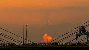 Dramatik bir günbatımı sıcak turuncu ışığı şehir köprüsünün üzerine saçar.