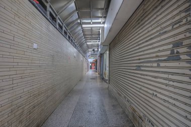 Bej kiremitli duvarlar, yuvarlanan panjurlar olan bir alışveriş merkezinde koridor.