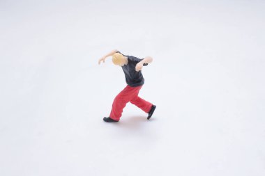 Minyatür bir oyuncak figürü temiz beyaz bir yüzey üzerinde amuda kalkıyor.