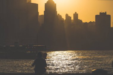 Siluetli figürler gün batımında tırabzanın kenarında duruyor, parıldayan bir şeye bakıyor, 16 Kasım 2025