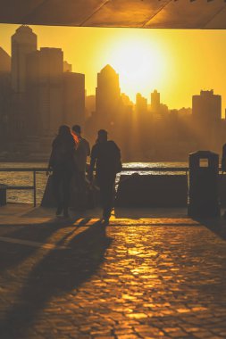 Ziyaretçi siluetleri altın bir günbatımına karşı duruyor. Yoğun bir şehir silueti, 16 Kasım 2025