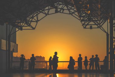 Siluetli ziyaretçiler, 16 Kasım 2025 'te gün batımında rıhtımda geziniyorlar.