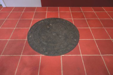 Büyük dairesel metal rögar kapağı kırmızı seramik üzerine kuruludur.