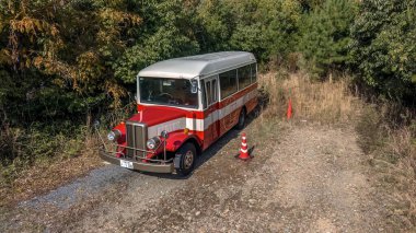 Beyaz otobüs, 24 Kasım 2025 'te uzun otlarla çevrili bir çakıl yolunda duruyor.