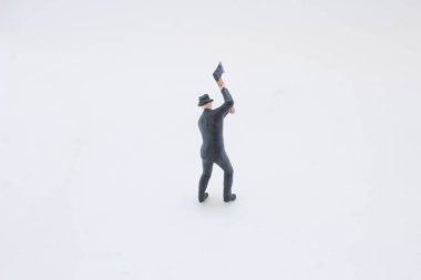 Siyah takım elbiseli küçük bir adam heykeli ve tahta saplı bir şapka kaldırıyor.