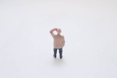Küçük plastik bir adam beyaz bir yüzeyde duruyor, kot pantolon giyiyor.