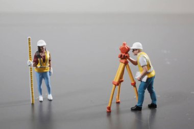 Küçük inşaat figürleri ölçüm araçları kullanarak arazi araştırması yapıyor