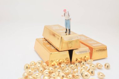 Tiny figurine surveys glittering gold bars surrounded by ingots