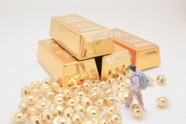 Tiny figurine stands near glittering gold bars on white backdrop