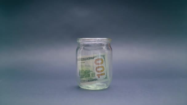 Женщина кладет 100 долларов США в стеклянную банку — стоковое видео