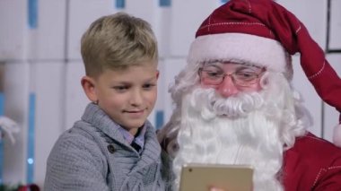 Küçük çocuk Noel babalar kucağına saygısız aracılığıyla Tablet sayfalarında oturur.