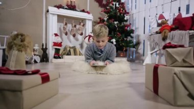 Yerde yatan ve dijital tablet ile kameranın oynadı küçük çocuk hamle bir çocuk, şömine ve Noel ağacı beyaz Oda
