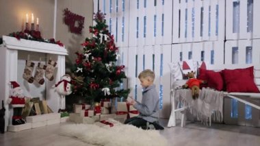 Noel ağacının yanında oturan bir çocuk, onu görme elinde akıllı telefon döner, Şömine ve Noel Ağacı ile beyaz Oda
