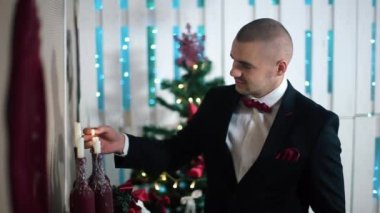 Siyah Takım Elbiseli Bir Adam Noel ağacı ile beyaz bir odada şömine üzerinde Mumlar Işıklar
