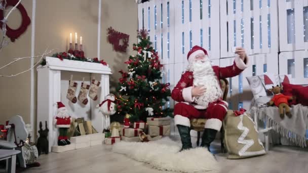 Santa gör Selfi sin Smartphone, rum med öppen spis och granen, presenter. — Stockvideo