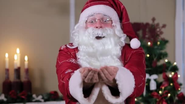 Santa waait sneeuw binnenshuis te Camera, kamer met open haard en kerstboom, geschenken. — Stockvideo