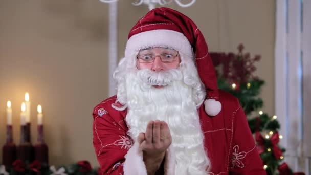 Santa Soplando nieve en la habitación con árbol a cámara, habitación con chimenea y árbol de Navidad, regalos . — Vídeo de stock