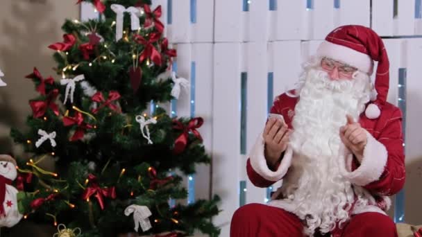 Papai Noel está trabalhando com o telefone, quarto com lareira e árvore de Natal, presentes . — Vídeo de Stock