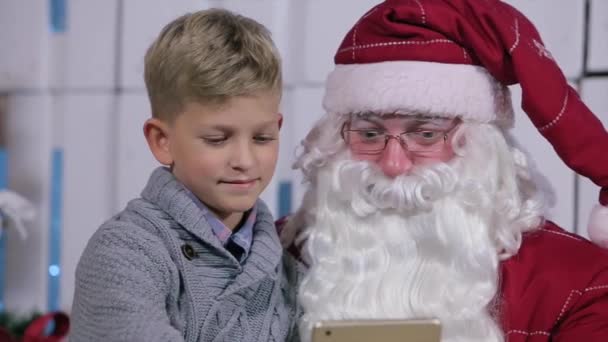 Niño se sienta en la vuelta de Santas, pasando a través de páginas en la tableta — Vídeos de Stock