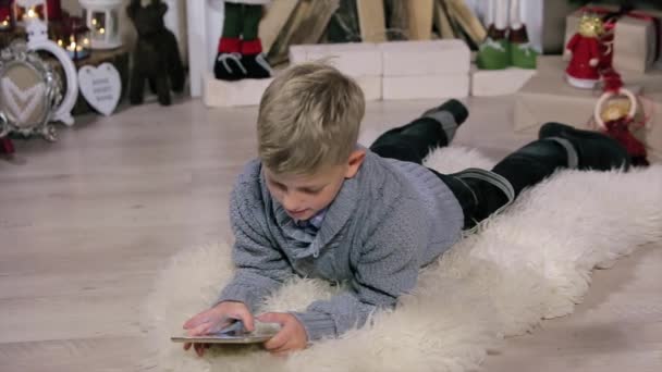 Ragazzino sdraiato sul pavimento, utilizzare display digitale, Sala bianca con camino e albero di Natale, Medio — Video Stock