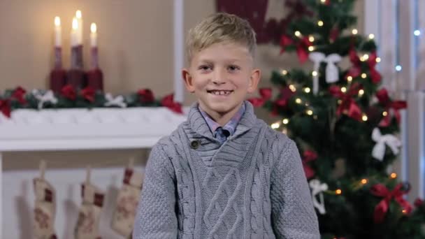 Menino segurando dois dedos, sorrindo, olhar câmera, quarto branco com lareira e árvore de Natal, Médio — Vídeo de Stock