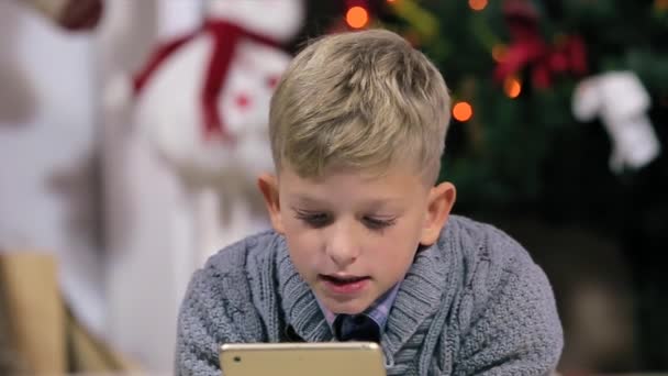 Kleine jongen liggend op de vloer, gebruik digitale display, witte kamer met open haard en kerstboom, close-up, mensen — Stockvideo