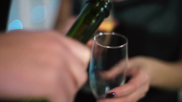 De man in het zwarte pak giet uit de fles, de vrouw in zwarte avondjurk houden van een glas — Stockvideo