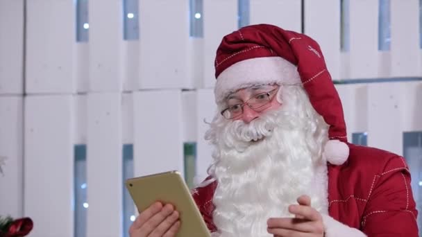 Papai Noel virando página no tablet digital no quarto com árvore de Natal e presentes — Vídeo de Stock