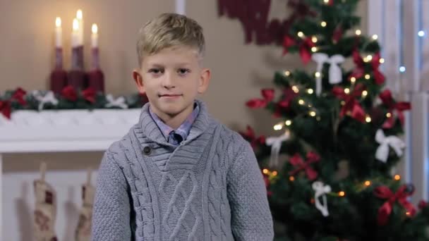 Felice espressivo ragazzo caucasico mostrando nella fotocamera i pollici in su segno sullo sfondo di Natale, sorridente, camera bianca con camino e albero di Natale, Medio — Video Stock